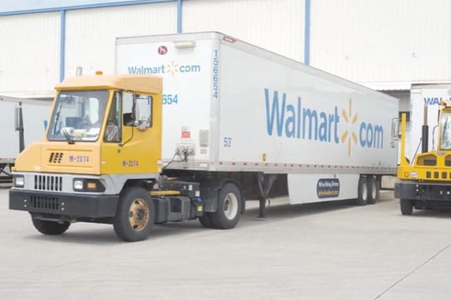Camión amarillo aparcado delante de un remolque de Walmart en el muelle de carga de un centro de distribución.