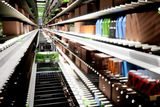 Estanterías de almacén con diversos productos y un sistema de recuperación automatizado que se desplaza por los pasillos.