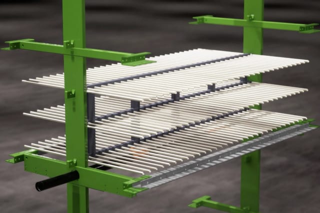 Estante metálico verde con varias barras horizontales blancas dispuestas en capas, utilizado para secar objetos sobre un fondo oscuro.