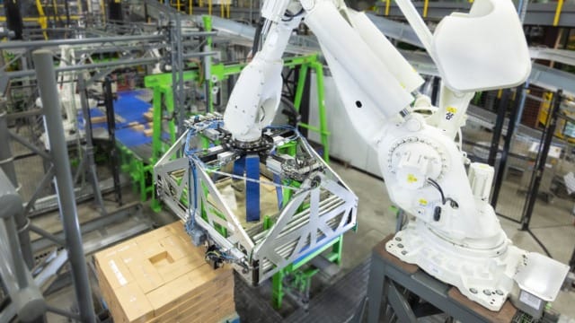 Un brazo robótico apila cajas en un moderno almacén, lo que pone de manifiesto la automatización en la logística industrial.
