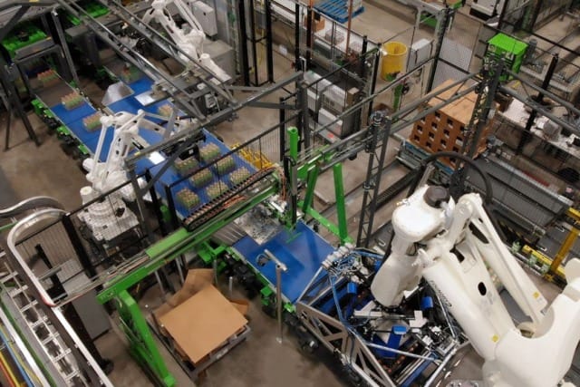 Línea de montaje robotizada en una fábrica moderna con maquinaria automatizada y cintas transportadoras que se encargan del manejo de materiales y productos.