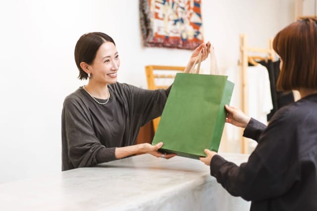 Un cliente recibe una bolsa de la compra verde de manos de un dependiente sonriente en el mostrador de una tienda.