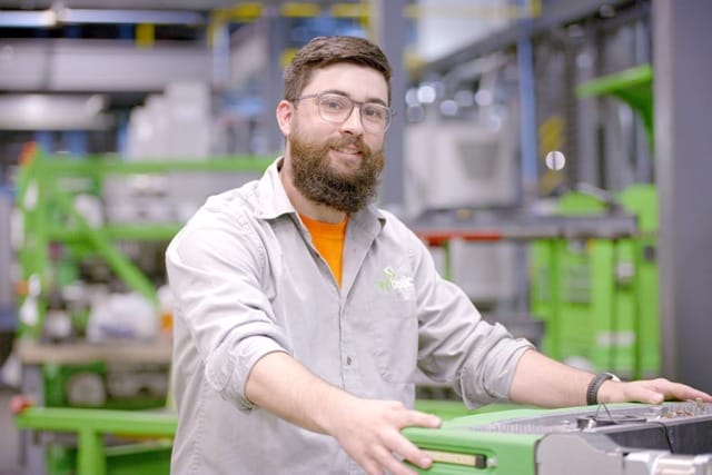 Hombre trabajando en un entorno industrial con maquinaria al fondo.