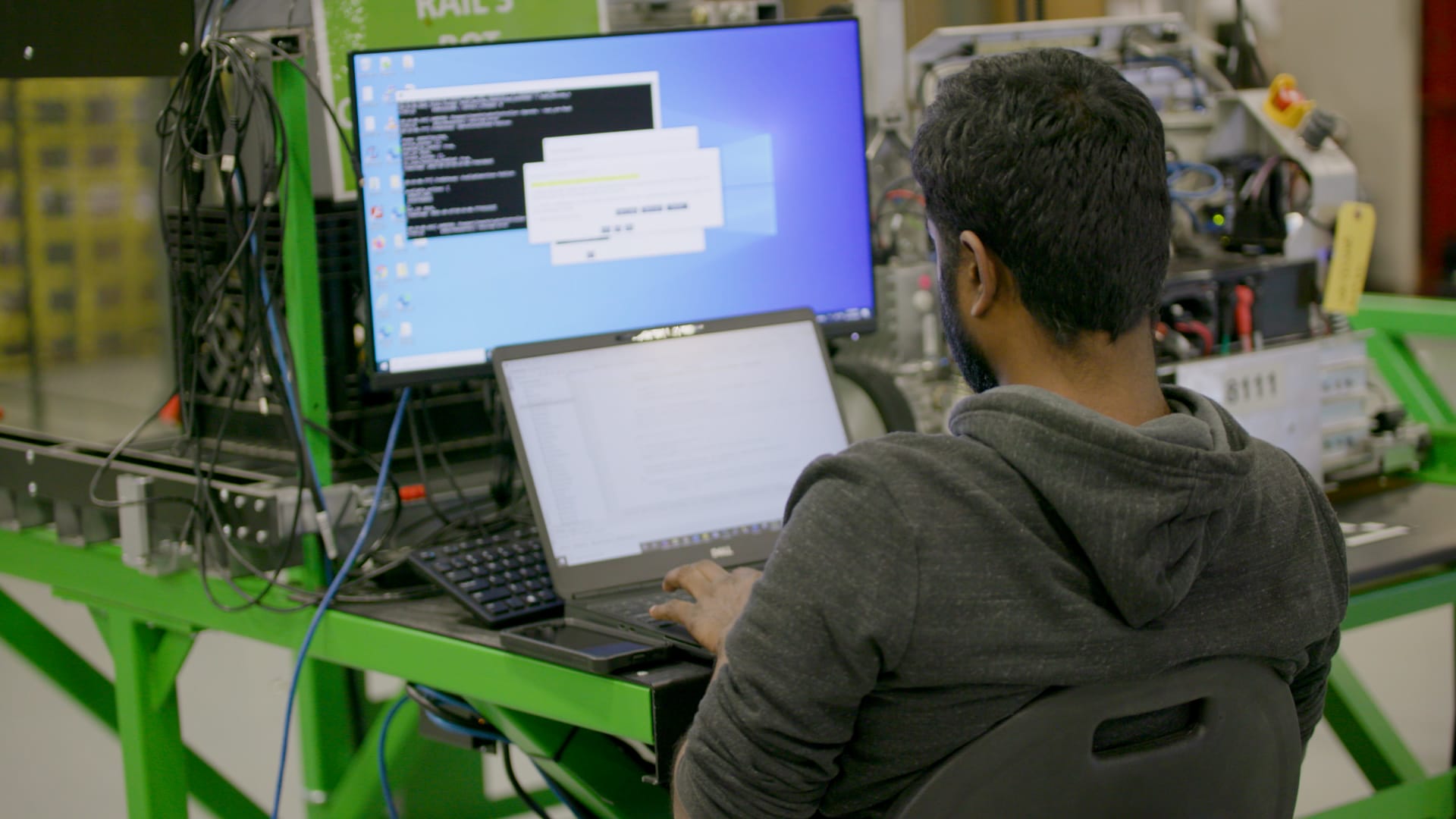 Persona trabajando en dos ordenadores con código en pantalla en un laboratorio de informática.