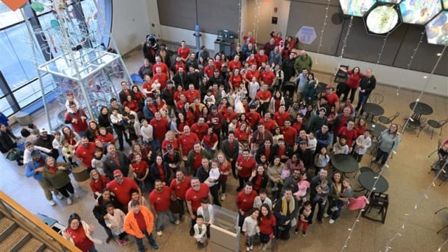 Un numeroso grupo de personas vestidas con camisetas rojas se reunió en una amplia sala con techos altos y una instalación decorativa.