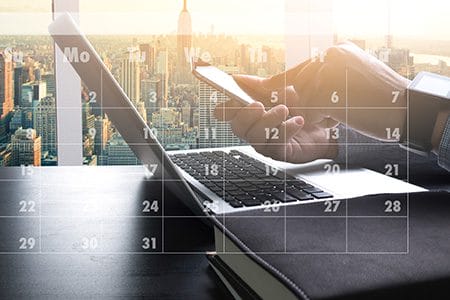 Persona utilizando un smartphone y un ordenador portátil con un calendario superpuesto en una oficina con vistas al perfil urbano de la ciudad.