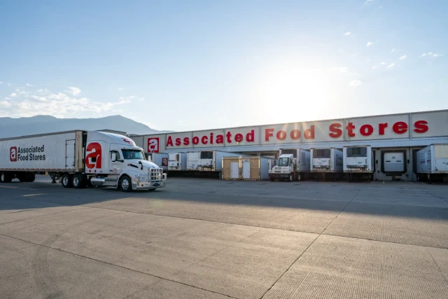 Truck parked outside Associated Food Stores warehouse with loading docks and sunny sky.