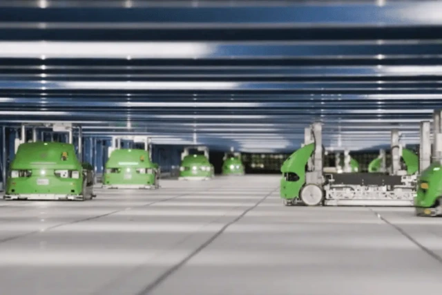 Robotic delivery carts moving in a large warehouse with high ceilings and evenly spaced horizontal beams.