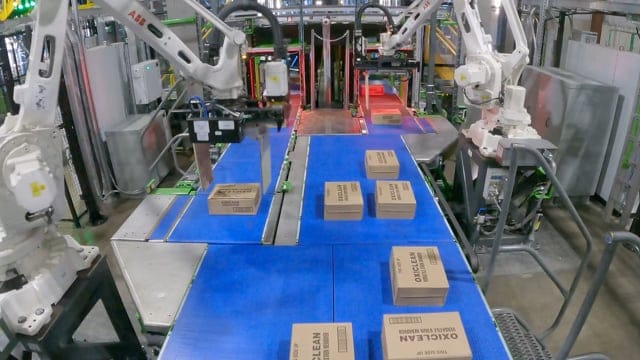 Các cánh tay robot đang phân loại các gói hàng trên băng chuyền trong một kho hàng, thể hiện công nghệ tự động hóa tiên tiến.