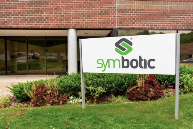 Biển hiệu công ty Symbotic đặt bên ngoài tòa nhà văn phòng hiện đại với khuôn viên được thiết kế cảnh quan và lối vào bằng kính.