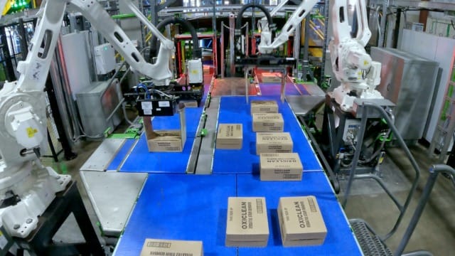 Các cánh tay robot đang phân loại và đóng gói các thùng carton trên băng chuyền trong một nhà máy công nghiệp.
