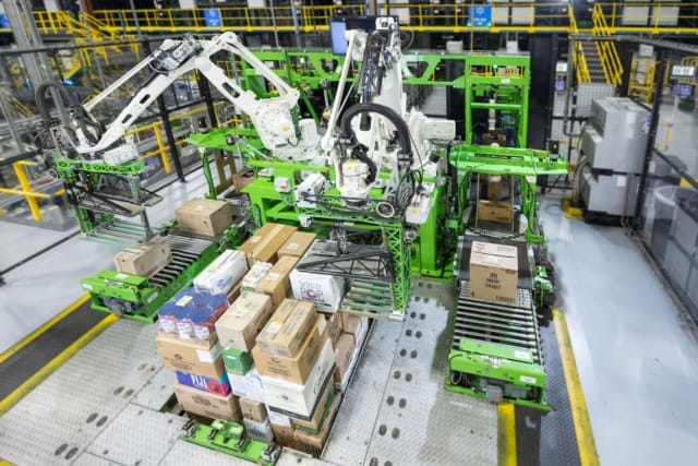 Các cánh tay robot đang phân loại và đóng gói thùng carton trong một kho hàng hiện đại.
